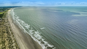 An aerial view of a beach with clear waters, a sandy shore, and a distant city skyline.