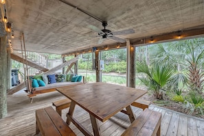 A wooden deck with a swing, a table, and a ceiling fan.