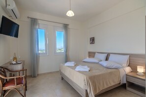 A hotel room with a bed, bedside table, chair, TV, window, and curtains.