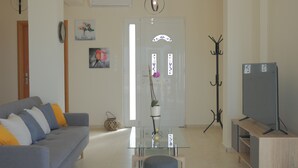 A living room with a sofa, a glass coffee table, a TV stand, and a coat rack.