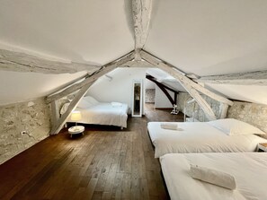 Acogedor dormitorio en ático con dos camas, suelo de madera y pared de piedra.
