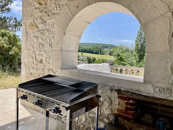 Estructura de piedra con una parrilla y vista a un paisaje verde.