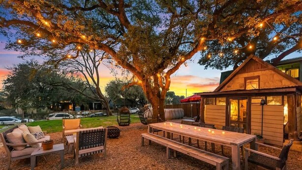 Un espacio al aire libre con mesa y bancos de madera, rodeado de árboles y luces colgantes.