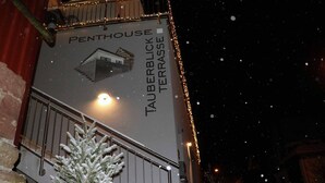 Señal que dice 'Penthouse Tauberblick Terrace' con una planta en maceta cubierta de nieve al frente.