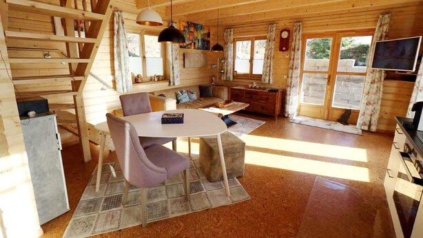 Un interior de cabaña acogedor, con comedor, cocina y una escalera.