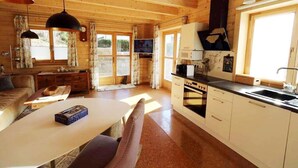 Interior acogedor de una cabaña con comedor, cocina y un amplio ventanal que deja entrar luz natural.