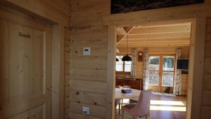 Interior de una cabaña de madera con comedor, cocina y una puerta visible.