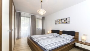 A modern bedroom with a wooden bed, a chandelier, a bedside table with a lamp, and a wall art piece. - Andy & Ida's Ferienwohnung (Neustadt an der Waldnaab)
