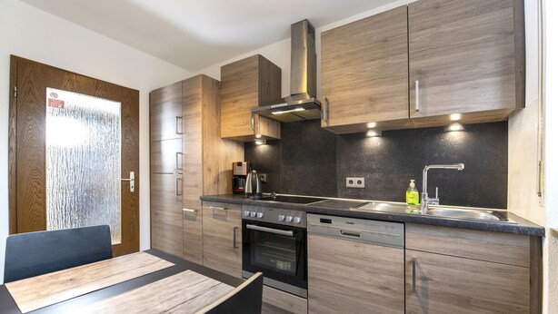 A modern kitchen with wooden cabinets, a stainless steel range hood, and a built-in oven. - Andy & Ida's Ferienwohnung (Neustadt an der Waldnaab)