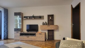 A modern living room with a flat-screen TV, wooden entertainment unit, and a sofa with a cushion. - Andy & Ida's Ferienwohnung (Neustadt an der Waldnaab)
