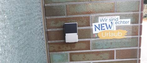 A brick wall with a security keypad and a sign that reads "Wir sind NEW Uraub".
