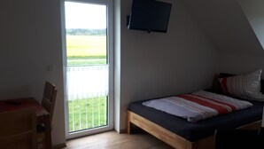 Un dormitorio con cama, una silla, un televisor y un balcón con vistas a un campo.