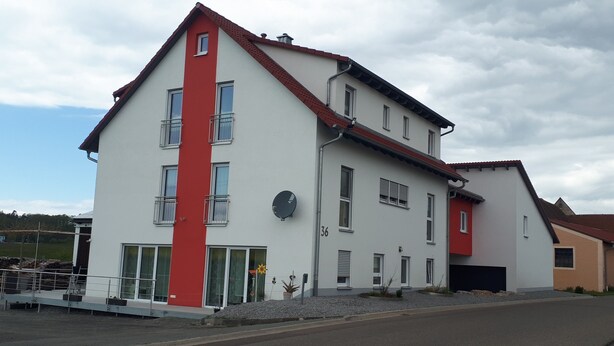 Un edificio de dos pisos con fachada roja y blanca, múltiples ventanas y una antena parabólica.