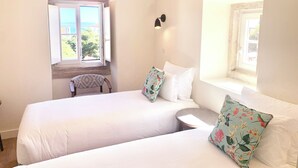 Une chambre avec deux lits, une petite table, une chaise et deux fenêtres donnant sur un paysage agréable.