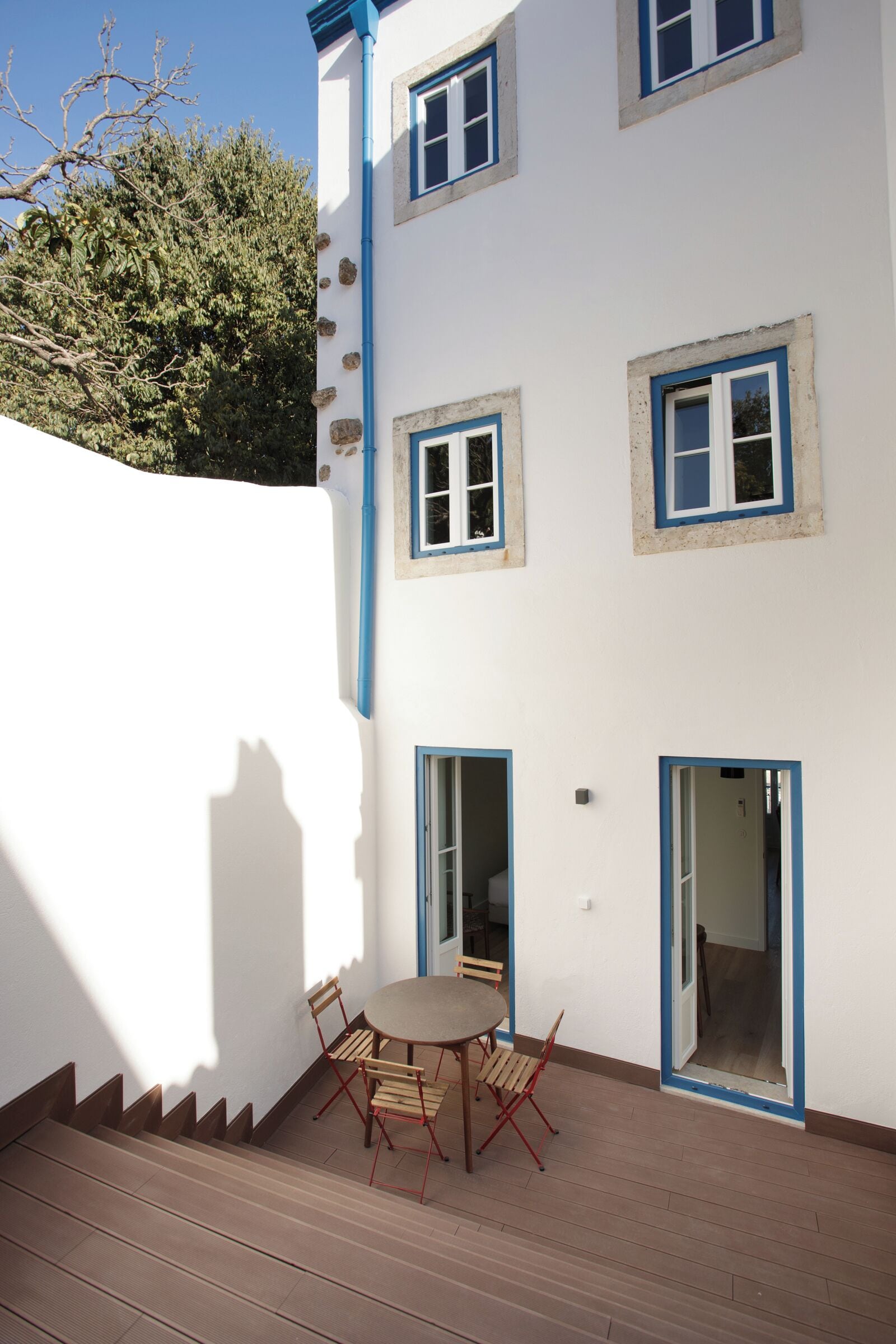 A white building with blue trim, a wooden deck, and a round table with chairs.