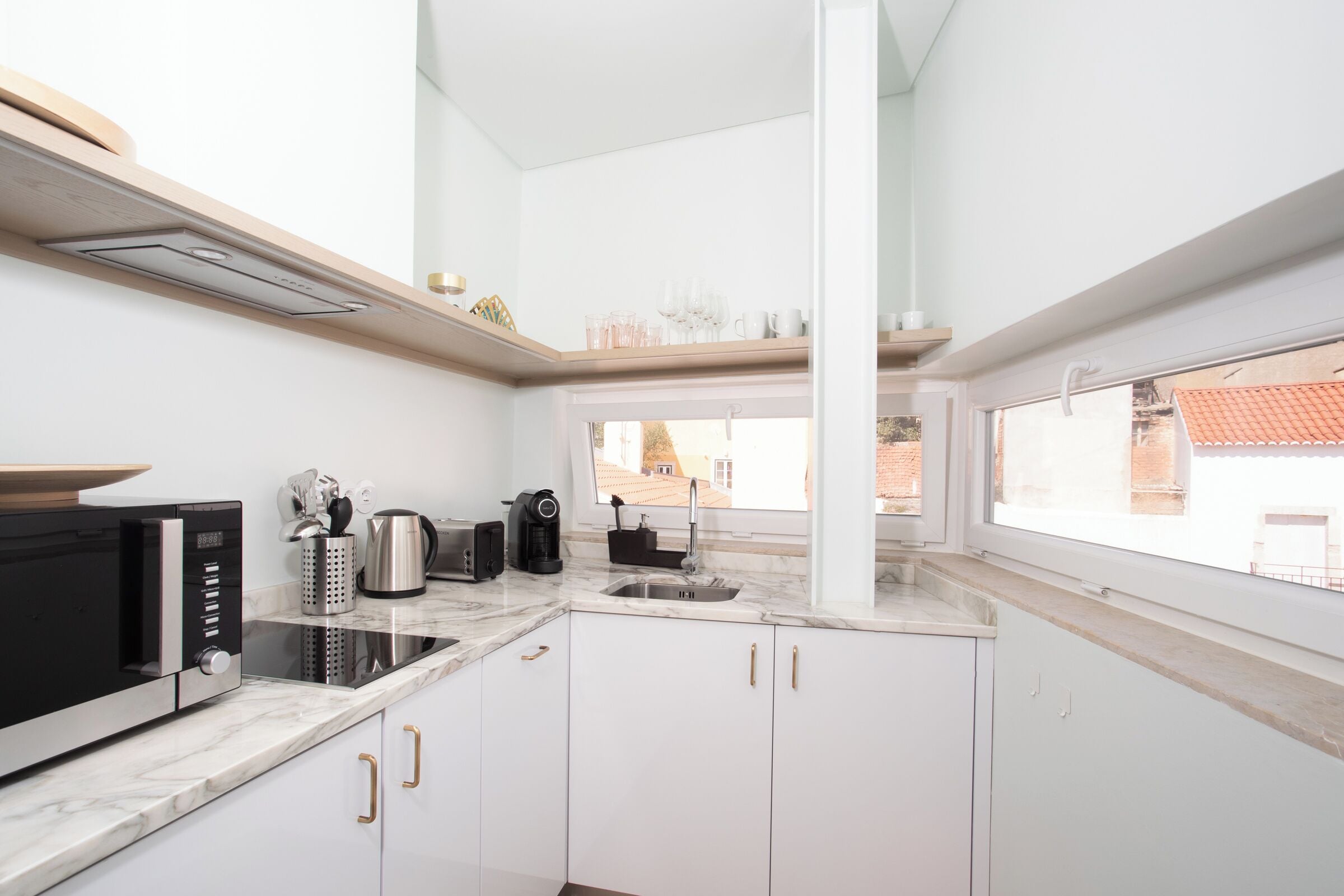 A modern kitchen with white cabinets, a black microwave, a coffee maker, and a window with a view of buildings.
