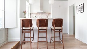 Une cuisine moderne avec trois tabourets de bar en bois, des armoires blanches et des luminaires suspendus.