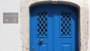 Une porte bleue ornée d’un motif décoratif sur la vitre, un bouton de porte en laiton et une enseigne au-dessus de la porte indiquant « Casa Saint Jorge ».