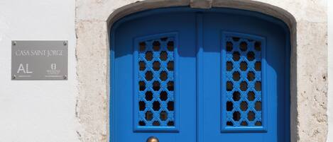 A blue door with a decorative window pattern, a brass doorknob, and a sign above the door reading "Casa Saint Jorge."