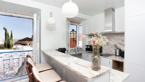 Une cuisine moderne dotée d’un plan de travail en marbre, d’une cuisinière encastrée et offrant une vue sur la mer grâce à une porte ouverte.
