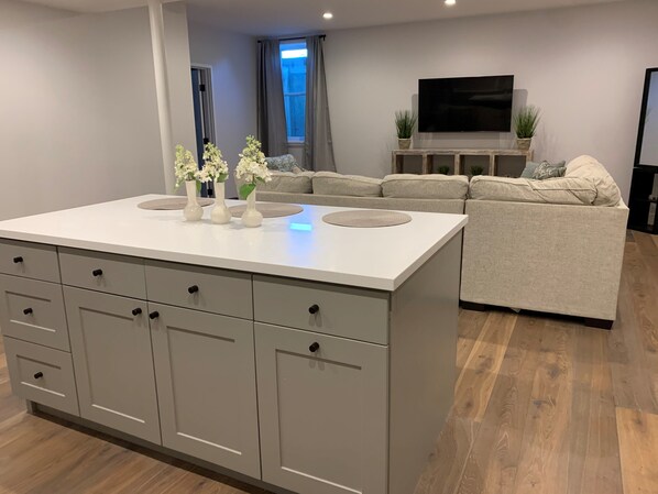 A modern living room with a central island, sofa, and a flat-screen TV. - Tranquilty (Nantucket)