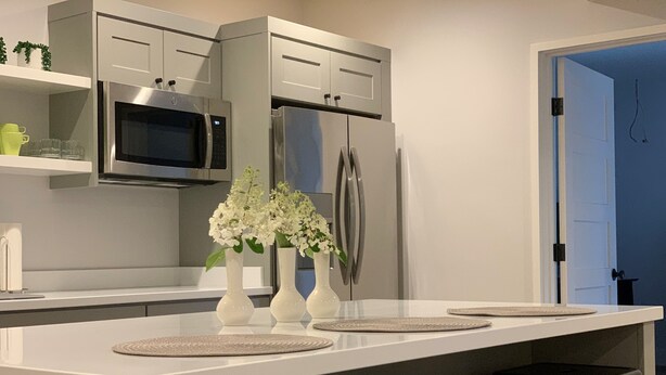 Una cocina moderna con armarios blancos, un refrigerador de acero inoxidable, un microondas y una isla central con tres jarrones blancos.