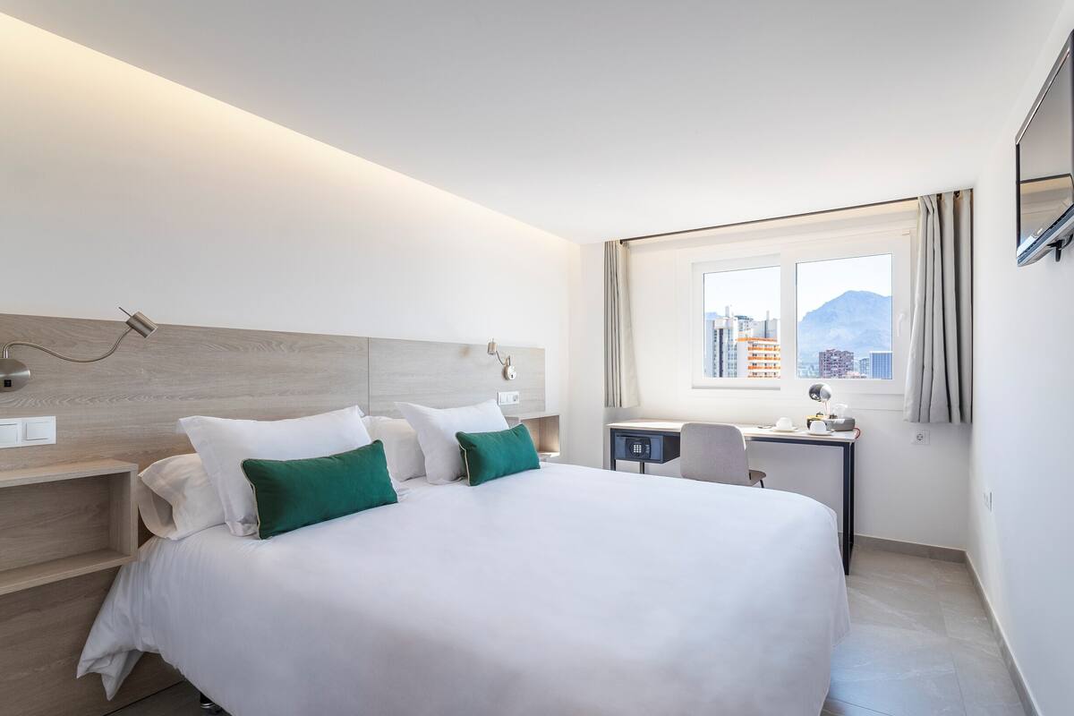 Una habitación de hotel moderna con una cama grande, un escritorio y una ventana con vistas a la ciudad.