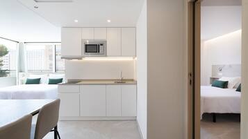 A modern hotel room with a kitchenette, a bed with green pillows, and a view of the city.