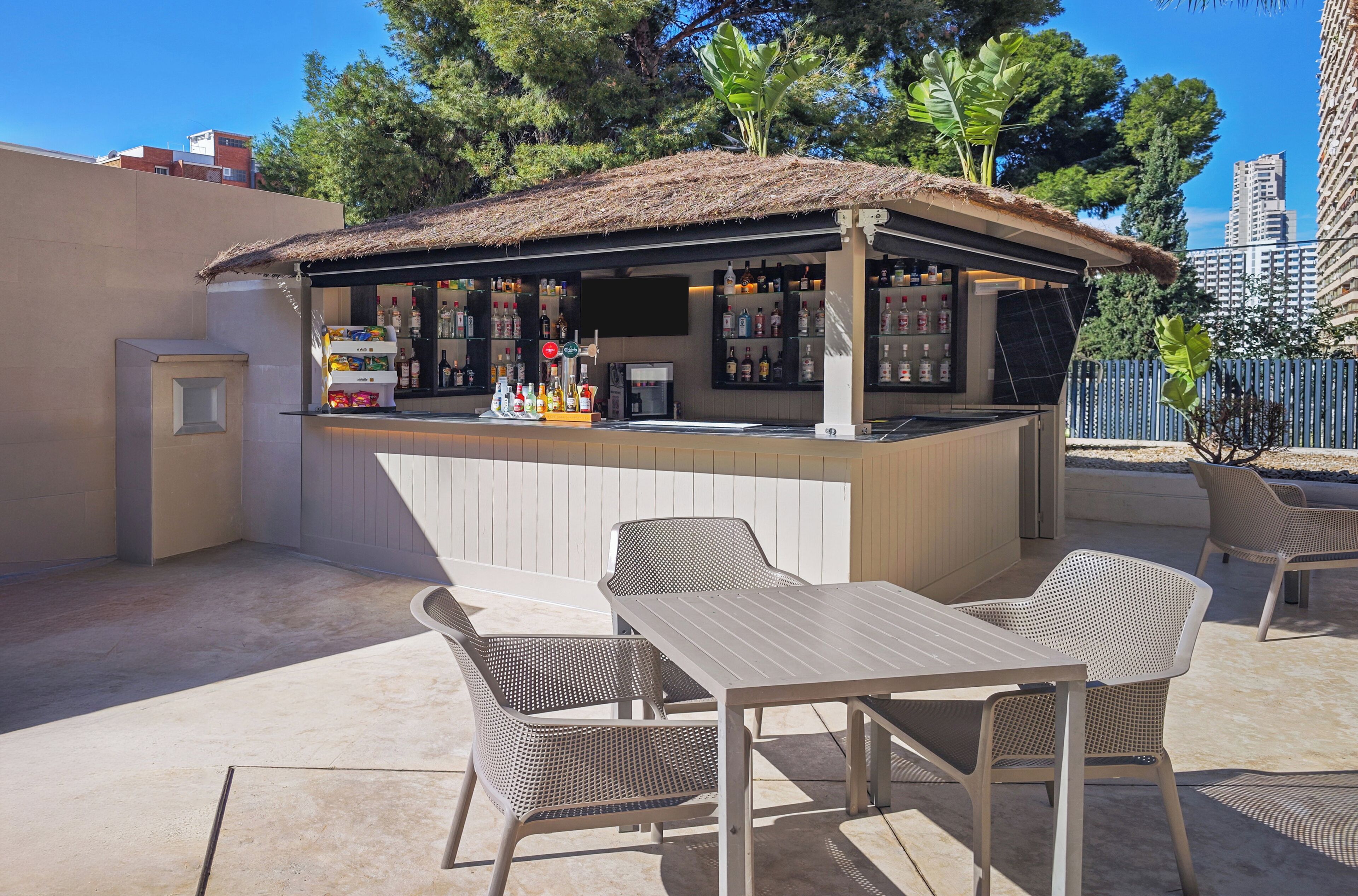 Un área de bar al aire libre con techo de paja, asientos y una variedad de botellas.