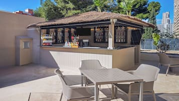 Un área de bar al aire libre con techo de paja, asientos y una variedad de botellas.