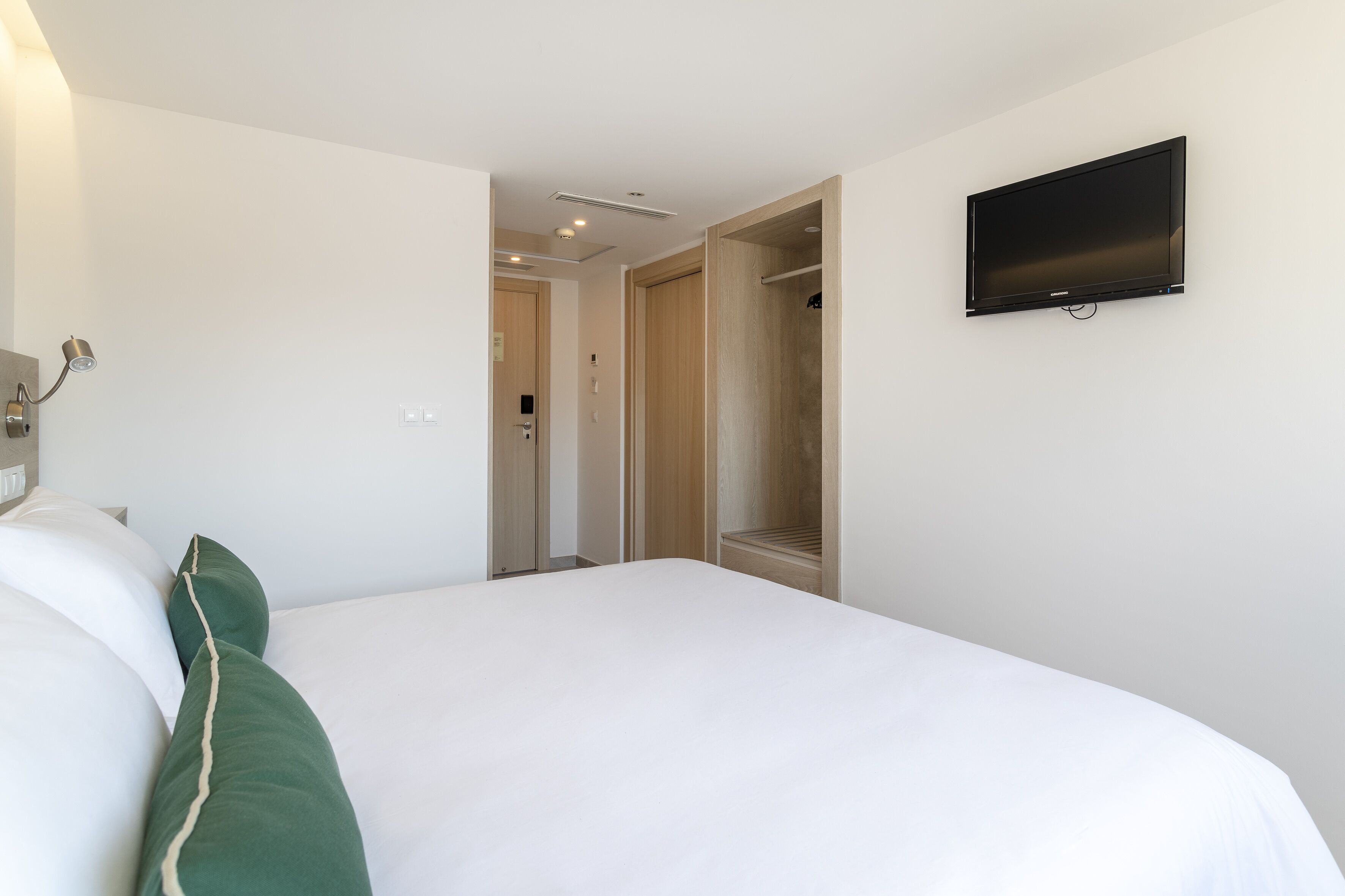 Una habitación de hotel con cama, televisión montada en la pared y vestidor.