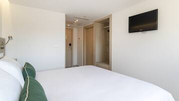 Una habitación de hotel con cama, televisión montada en la pared y vestidor.