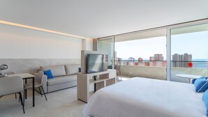 Een moderne hotelkamer met een bed, een bank, een televisie en een balkon met uitzicht op de stad.