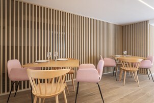 Un comedor moderno con mesas de madera y sillas rosas, que presenta listones verticales de madera en la pared.