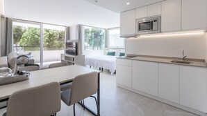 Een moderne keuken met witte kasten, een magnetron en een spoelbak. Er is een eethoek met een tafel en stoelen.