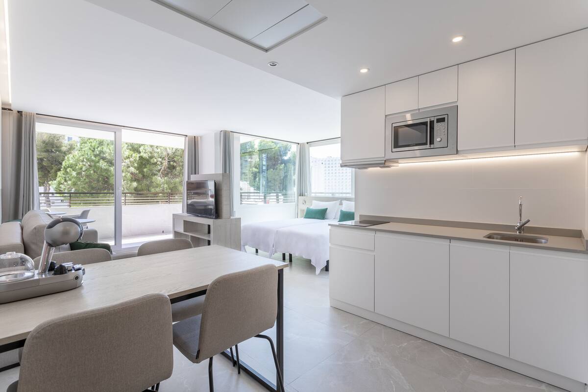 Una cocina moderna con armarios blancos, un microondas y un fregadero. Hay una zona de comedor con una mesa y sillas.