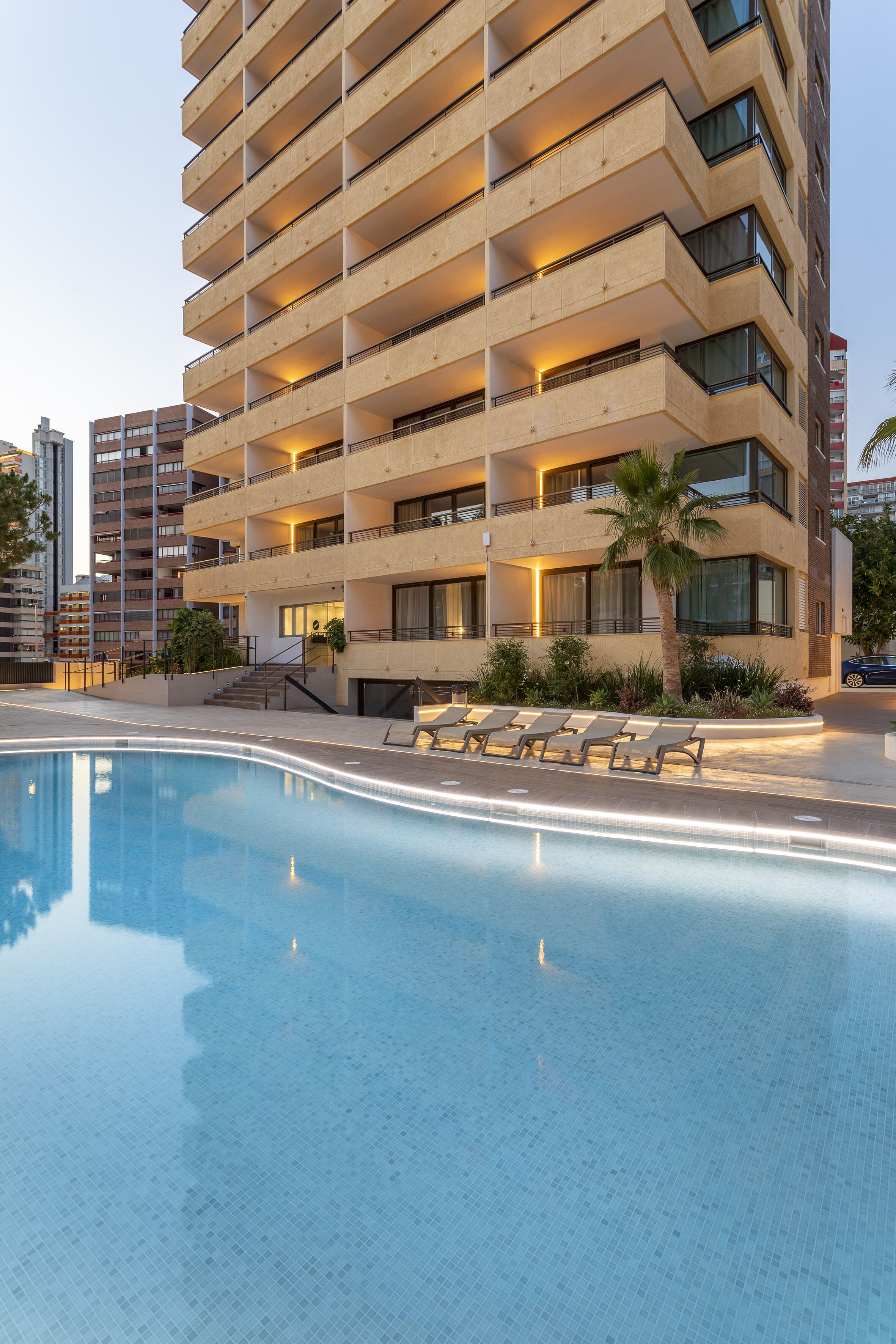 Ein modernes Hotel mit Schwimmbad, mehreren Balkonen und einer Palme.