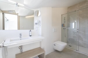 A modern bathroom with a white sink, a mirror, a toilet, and a glass-enclosed shower.