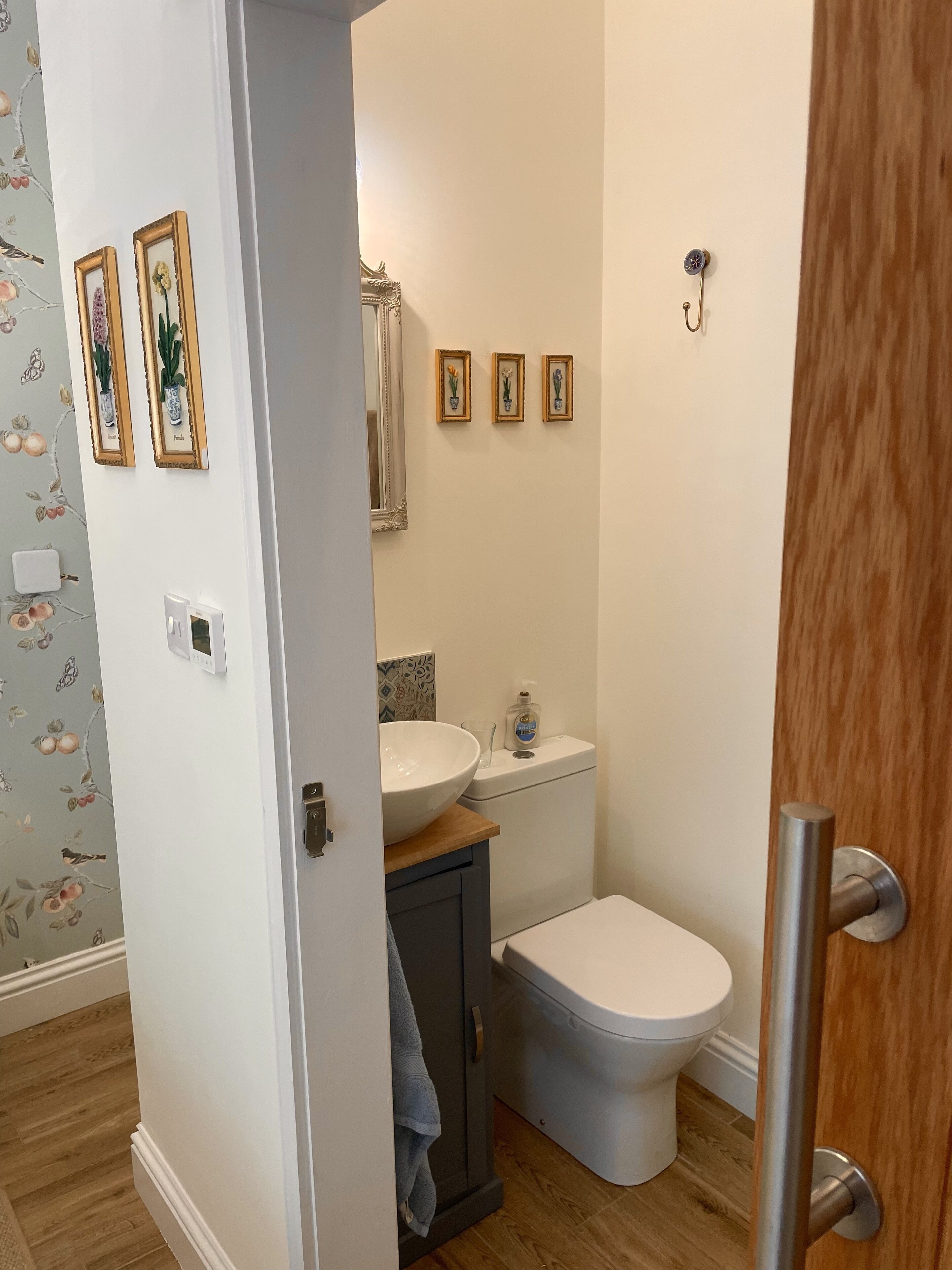 Un baño con inodoro blanco, tocador de madera con un lavamanos grande y zona de ducha. Hay tres cuadros enmarcados en la pared sobre el tocador.