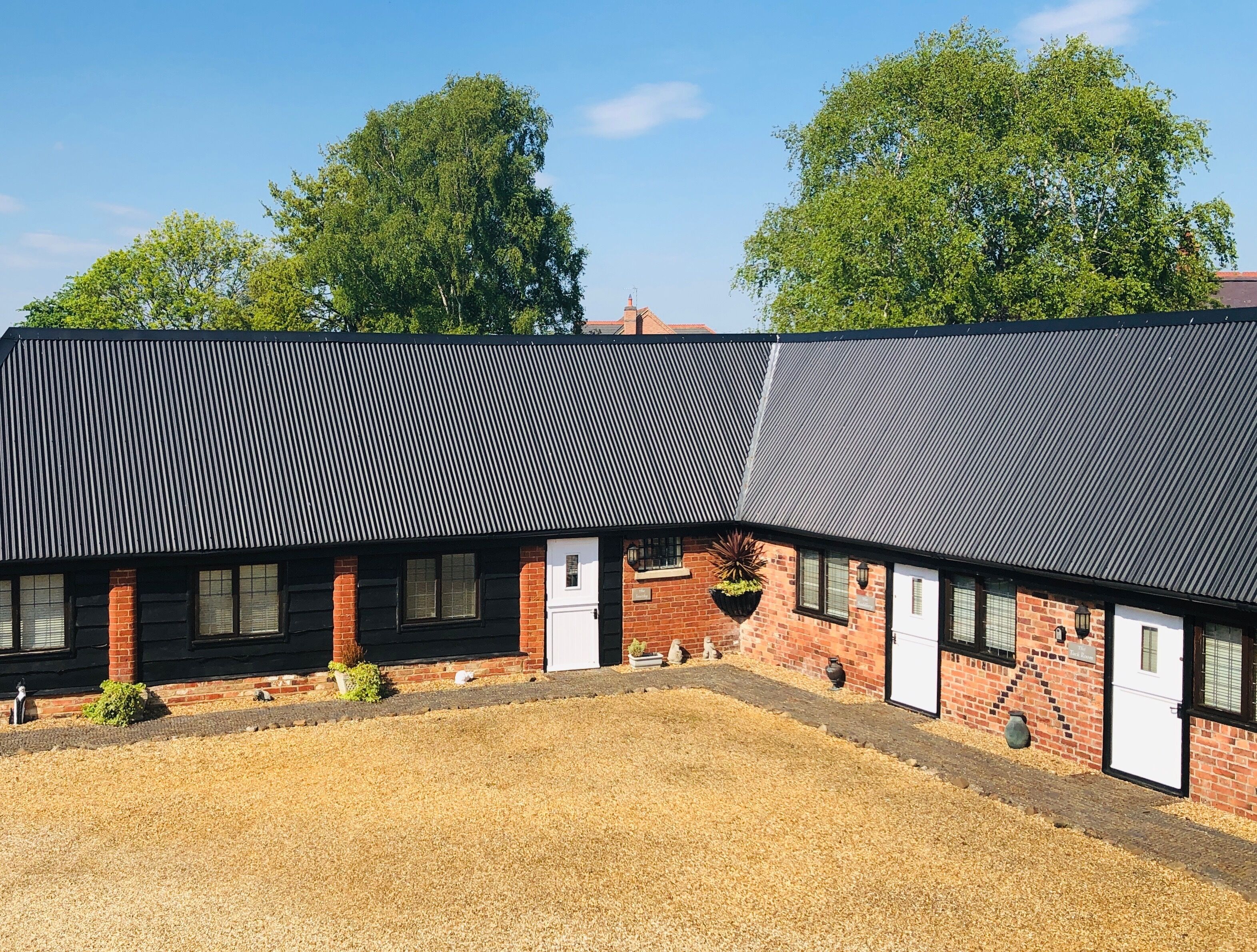A building with a corrugated metal roof, brick walls, and a gravel courtyard.