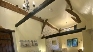 A bedroom with a large bed, wooden beams, a chandelier, and a window with blinds. - Hunt House Quarters (Rugby)