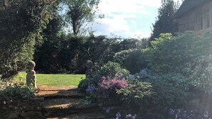 A garden with stone steps leading to a grassy area, surrounded by various plants and flowers. - Hunt House Quarters (Rugby)