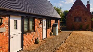 A brick building with a white door and windows, a gravel driveway, and a smaller brick building in the background.
