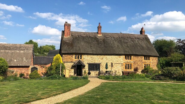 A traditional stone house with a thatched roof, a gravel path leading to the entrance, and a small garden area. - Hunt House Quarters (Rugby)