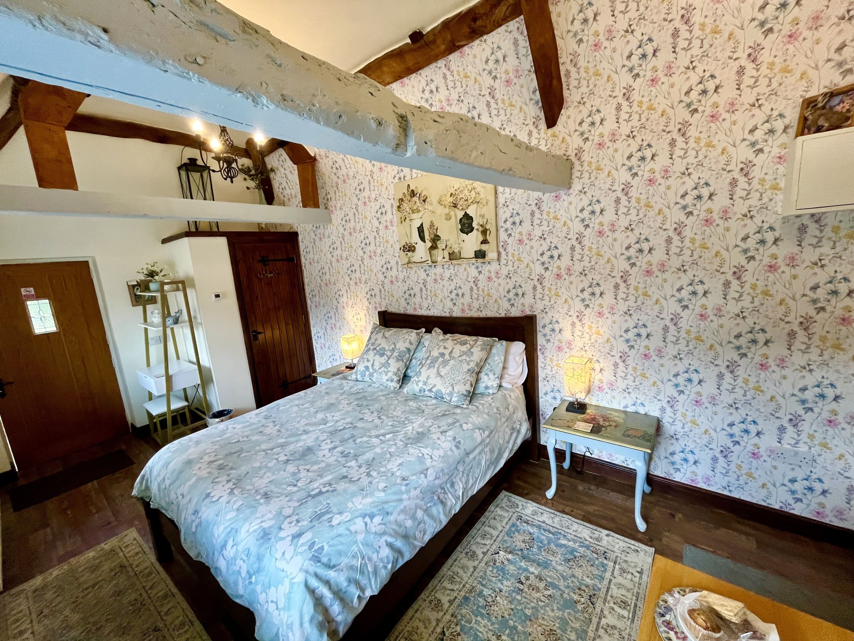 Un dormitorio con cama de madera, papel tapiz floral, una mesita de noche y una alfombra.