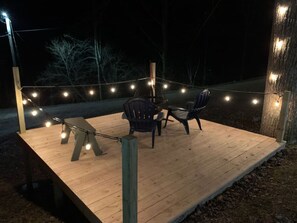 Eine Holzterrasse mit Lichterketten, zwei Stühlen und einem Tisch.
