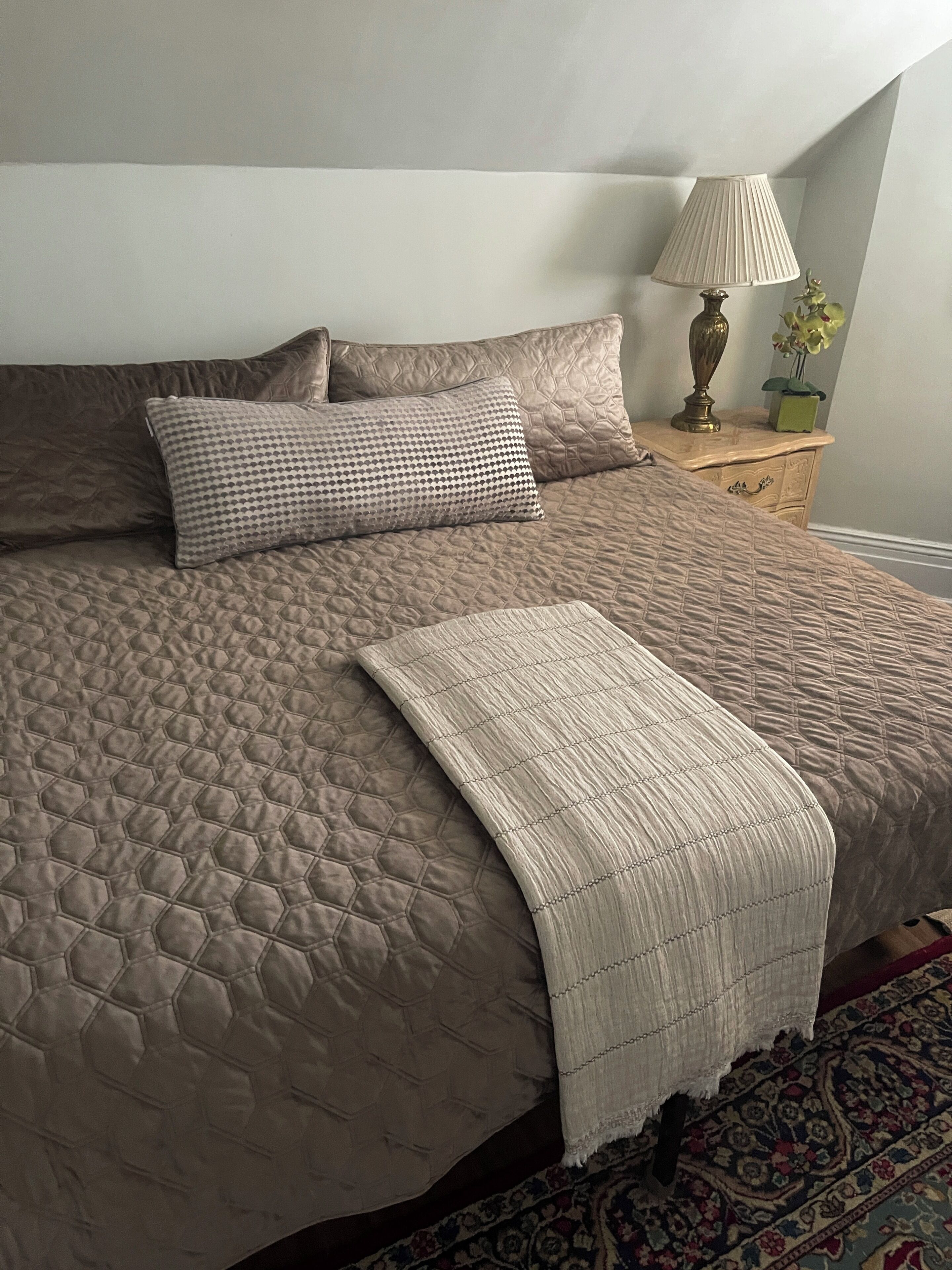 A bed with a quilted headboard, a bedside table with a lamp, and a small plant.