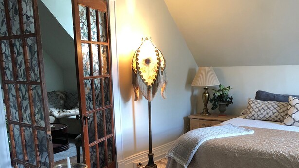 A cozy bedroom with a bed, bedside table, lamp, and a view of a balcony.