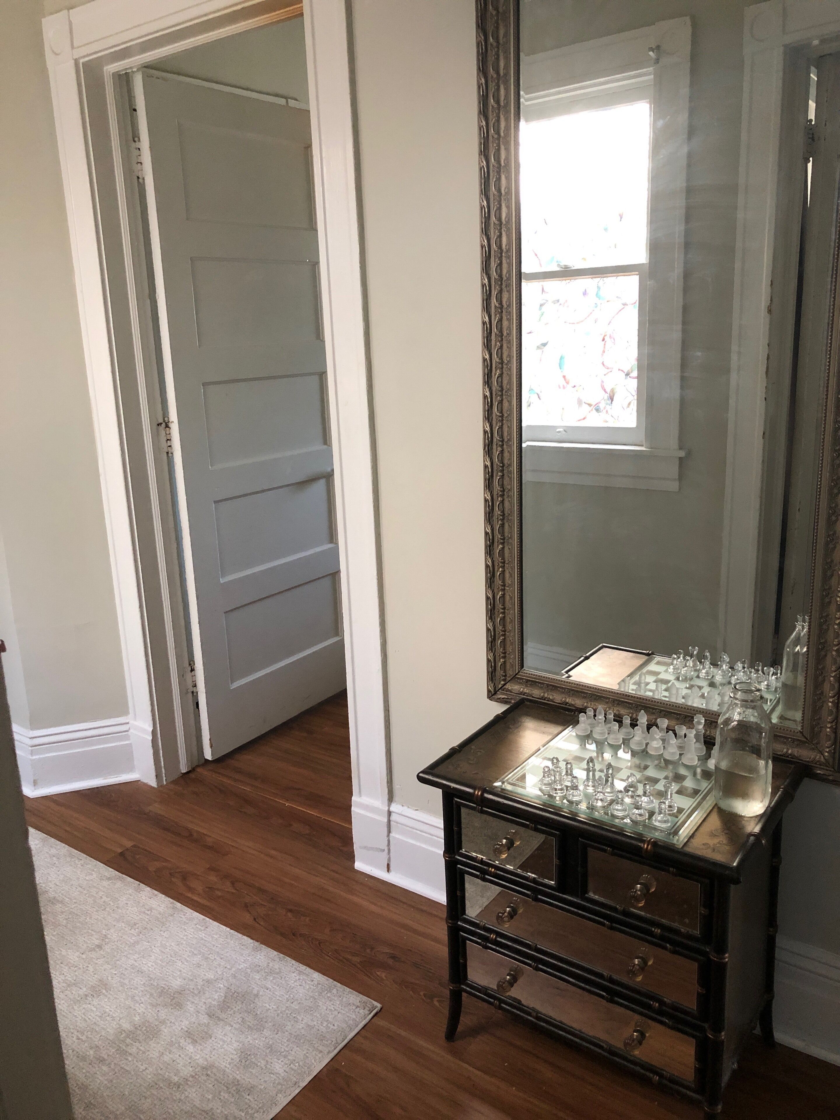 A room with a wooden floor, a glass chess table, a mirror, and a door.