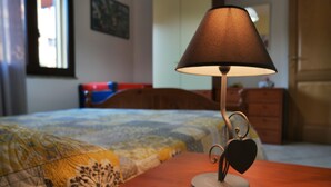 A bed with a patterned quilt, a bedside table with a lamp, and a dresser in a room with a window and a painting on the wall. - Central Porto San Paolo, 2 bedrooms, 6 beds, Wi-fi, air conditioning (Porto San Paolo)